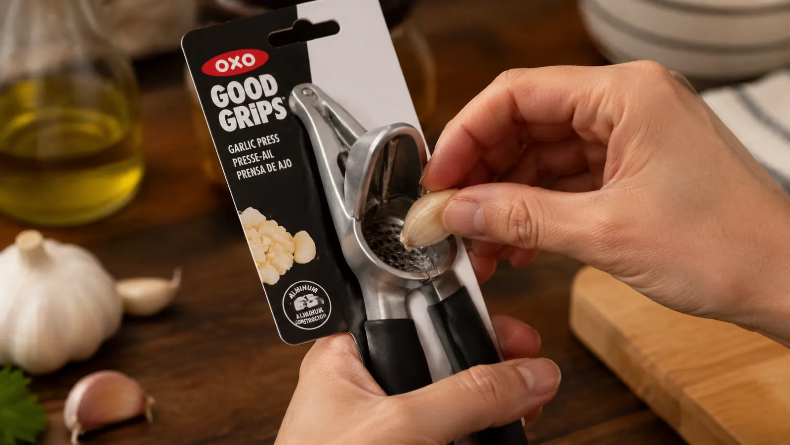 Hand placing an unpeeled garlic clove into the basket of the OXO garlic press before squeezing