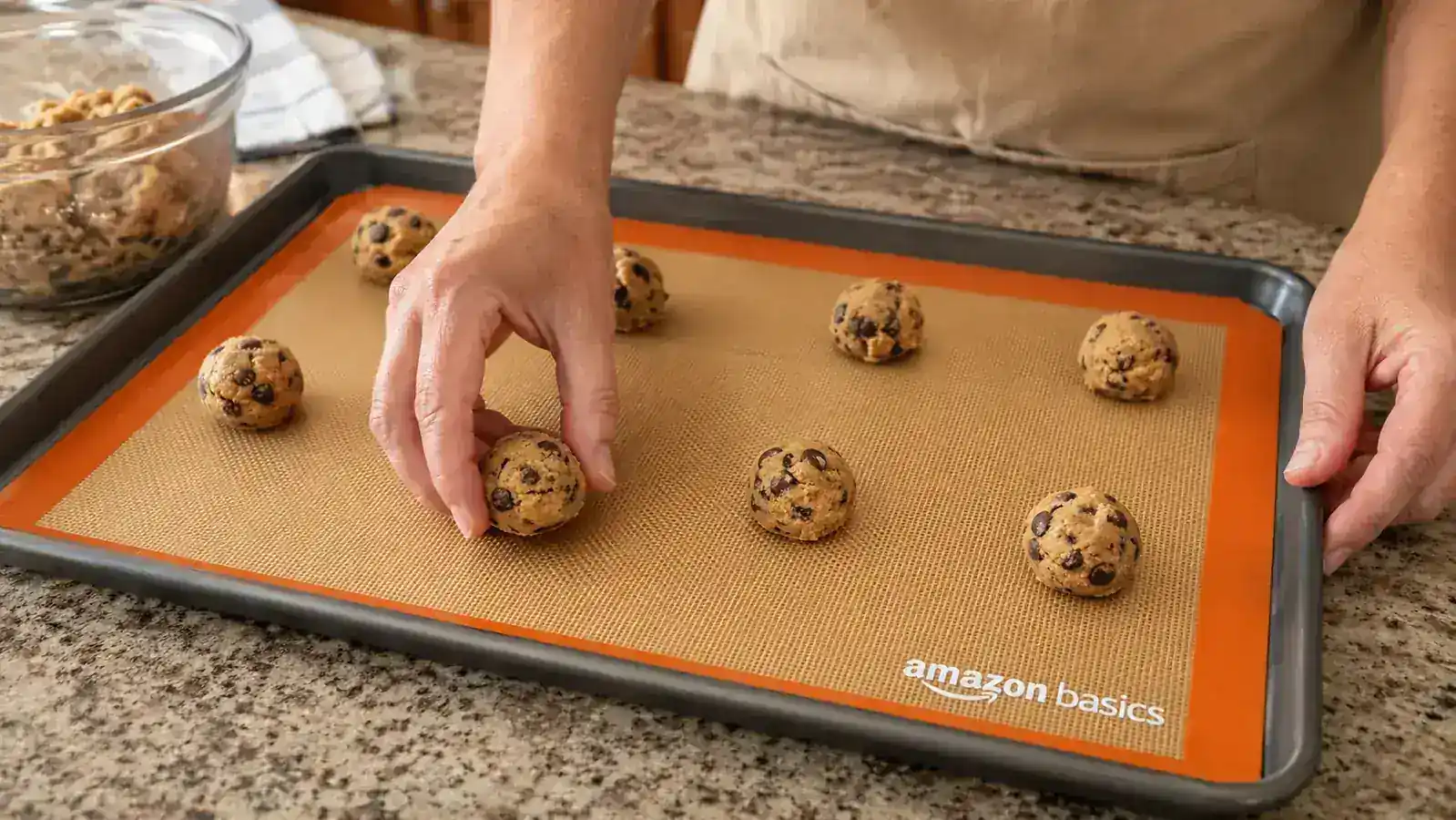 Hand placing raw cookie dough balls onto an Amazon Basics silicone baking mat on a sheet pan