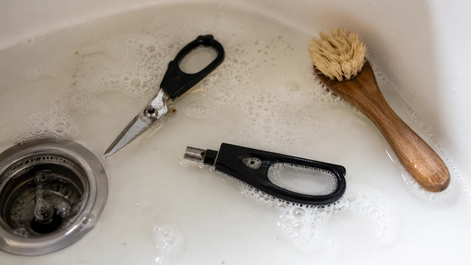 Kitchen shears disassembled into two separate blades in a sink of soapy water for cleaning