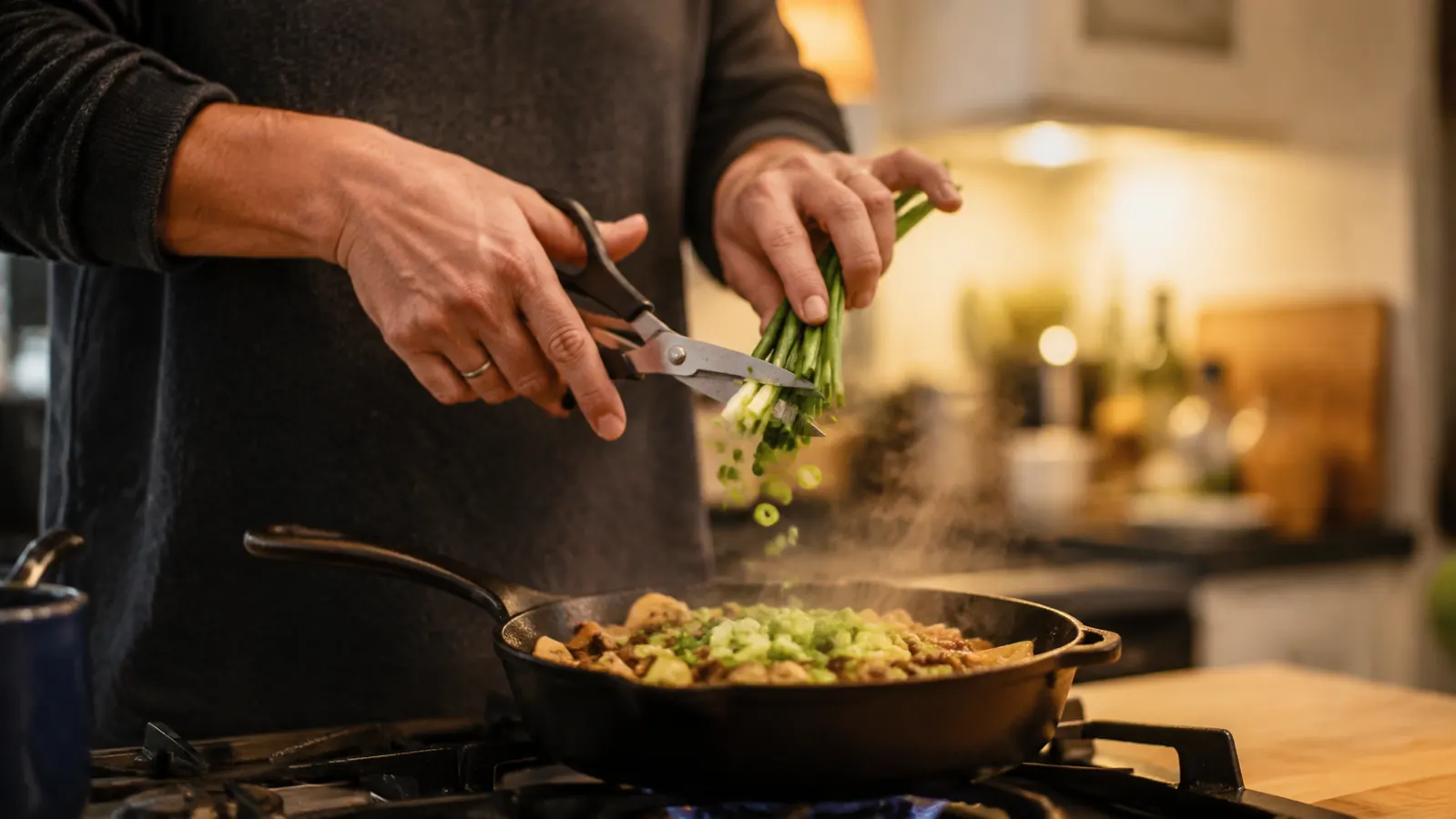 Home cook snipping fresh scallions directly over a hot skillet on the stovetop