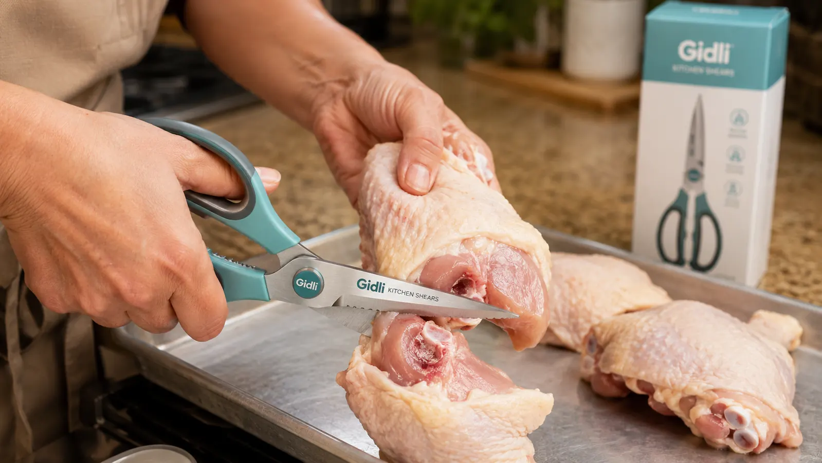 Hands using kitchen shears to cut raw chicken thigh directly over a sheet pan