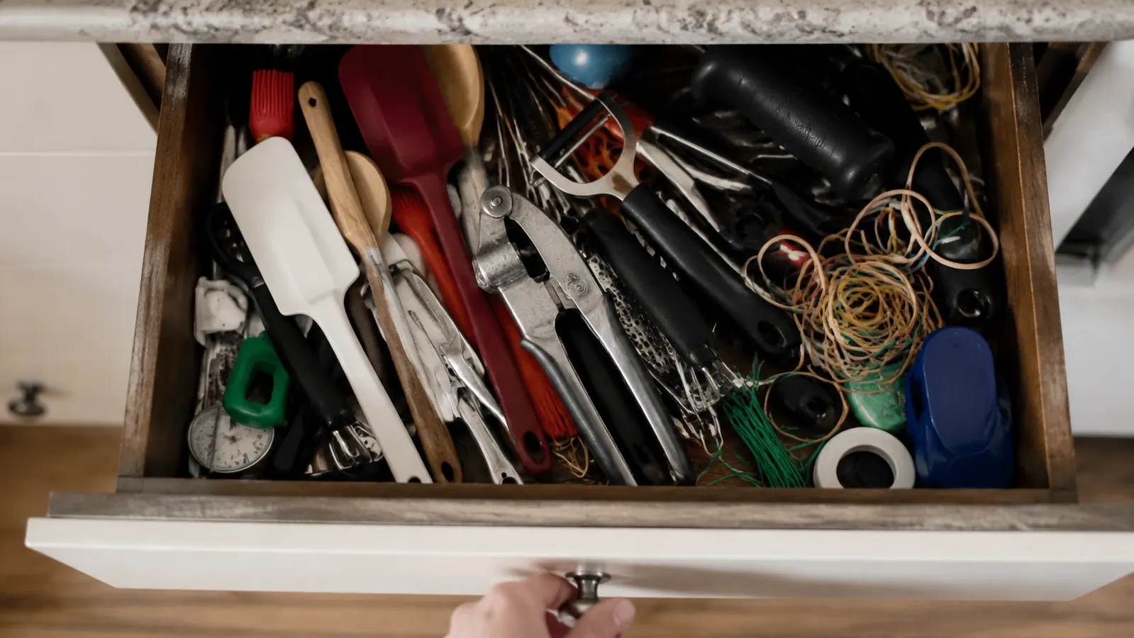 Garlic press sitting unused in a cluttered kitchen drawer filled with other gadgets
