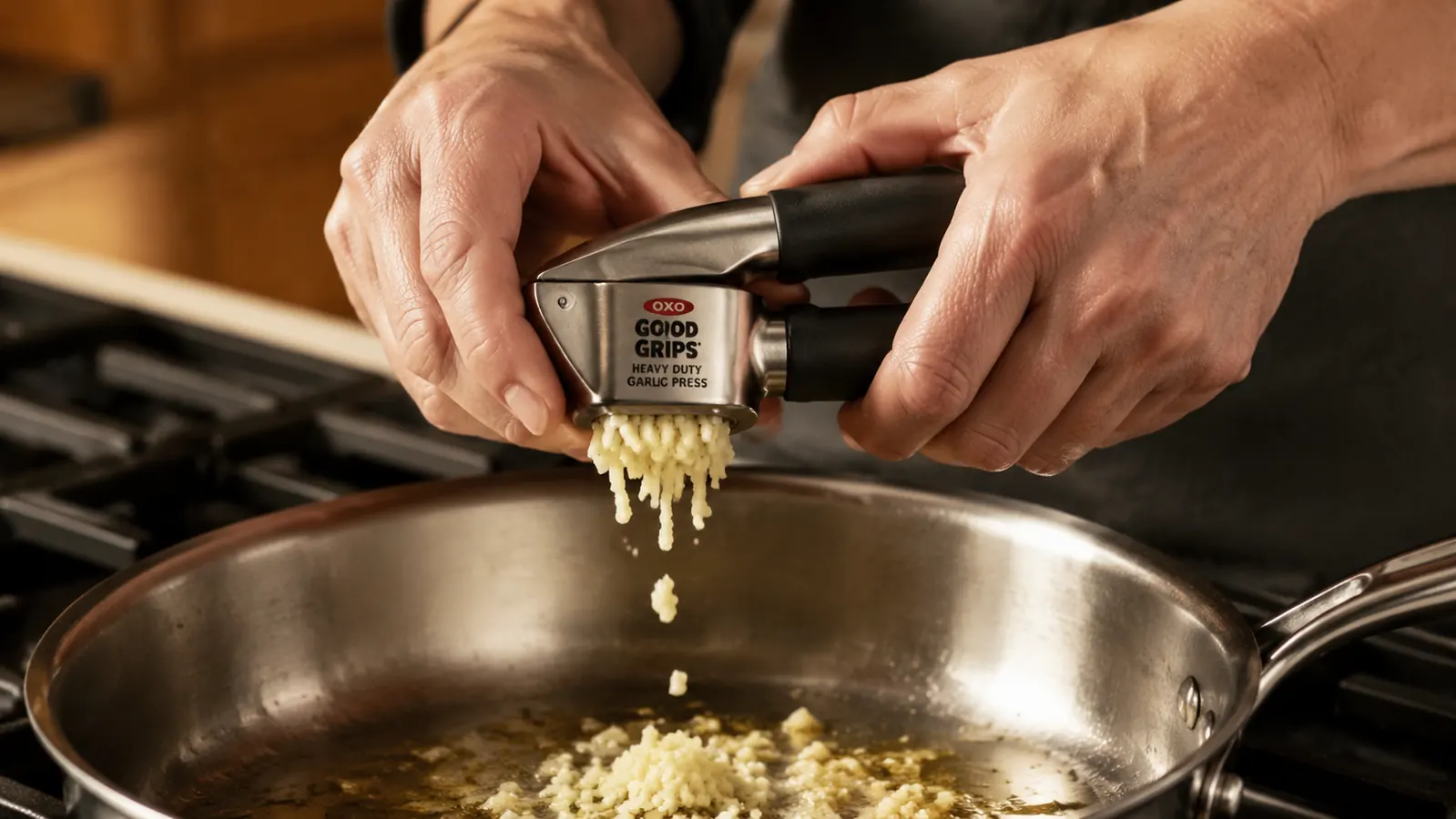 Hand squeezing the OXO garlic press directly over a saute pan with minced garlic falling through